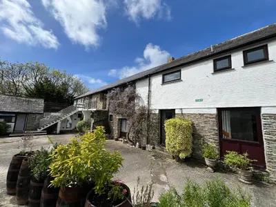 a white building with potted plants in front of it at Malt-Barn Conversion, with access to Pool & Hot Tub-at Fox Valley Cottages in Lansallos