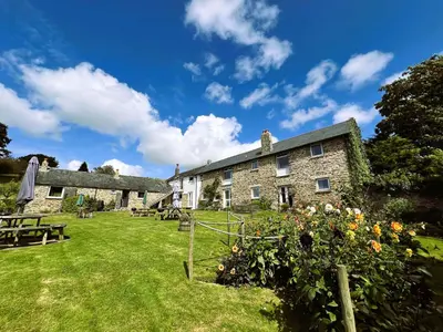 a large stone building with a yard with tables and flowers at Malt-Barn Conversion, with access to Pool & Hot Tub-at Fox Valley Cottages in Lansallos
