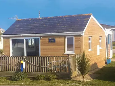 a small wooden house with a wooden fence at Clonmore Beach Chalet, Riviere Towans in Hayle