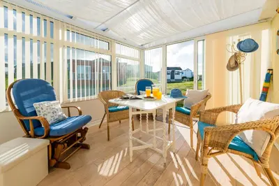 a room with a table and chairs and windows at Clonmore Beach Chalet, Riviere Towans in Hayle
