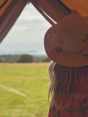 a woman wearing a hat looking out of a window at Furnished Bell Tent 4 in St Austell
