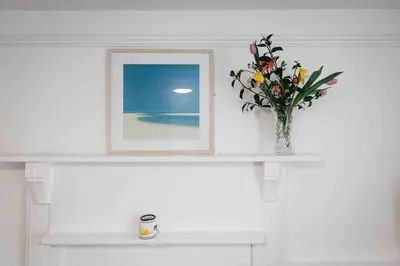 a shelf with a vase of flowers and a picture at flat with Cornish charm, parking and garden in St Ives