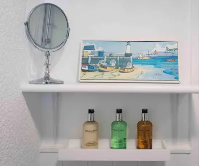 a shelf with three bottles of soap and a mirror at flat with Cornish charm, parking and garden in St Ives
