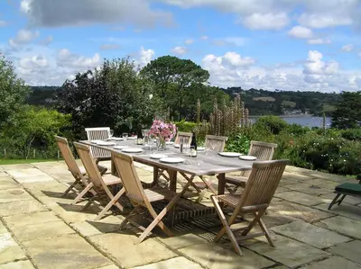 a wooden table with chairs and flowers on a patio at Penarvon House - Stunning Waterfront Escape with Games Room in Manaccan