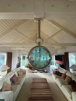a large clock hanging from the ceiling of a living room at Penarvon House - Stunning Waterfront Escape with Games Room in Manaccan