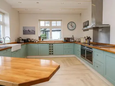 a kitchen with blue cabinets and a wooden table at Penarvon House - Stunning Waterfront Escape with Games Room in Manaccan