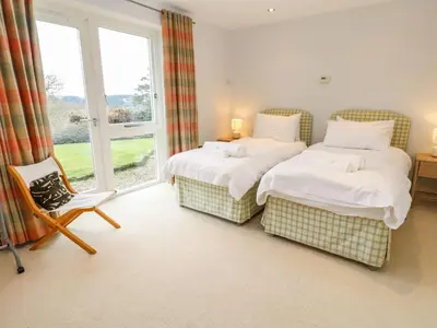 a bedroom with two beds and a chair and a window at Penarvon House - Stunning Waterfront Escape with Games Room in Manaccan