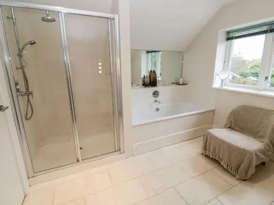 a bathroom with a shower and a tub and a chair at Penarvon House - Stunning Waterfront Escape with Games Room in Manaccan