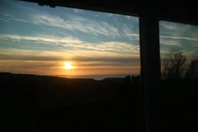 a view of the sunset through a window at Bay View Cottage - Amazing sea views and 3 bedrooms Sleeps 6-8 in Treknow