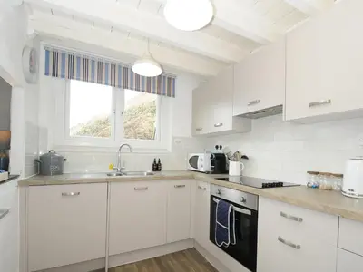 a white kitchen with white cabinets and a window at Little Ruffo in Tintagel