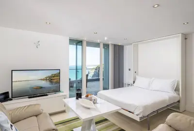 a white bedroom with a bed and a tv at 25 Rocklands in Newquay in Newquay