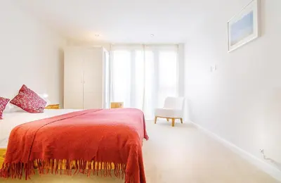 a white bedroom with a bed and a chair at Cinq 5 Zinc in Fistral, Newquay in Newquay