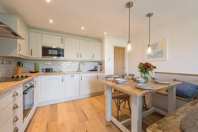 a kitchen with white cabinets and a wooden table at Sandcastles 11 Europa Court in Mawgan Porth in Mawgan Porth