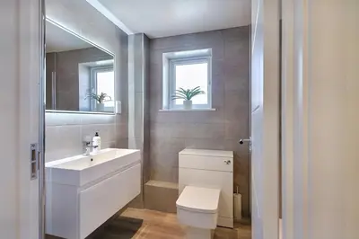 a bathroom with a sink and a toilet and two windows at 2022 Modern Home In Central Hayle With Parking & EV plug in Hayle