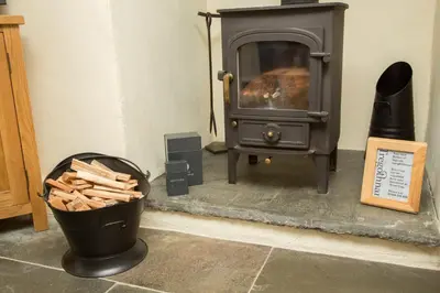a wood stove in a room with a bucket of wood at Riverside in Kea
