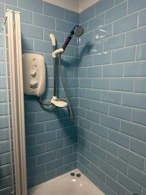 a blue tiled bathroom with a shower and a toilet at Penolva Beach Side Apartment in Perranporth