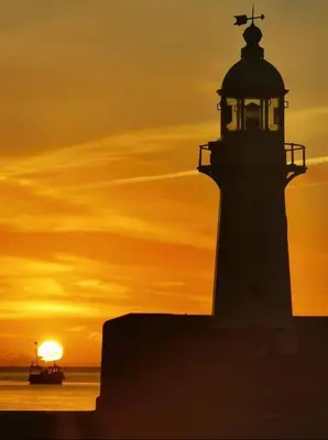 a lighthouse at sunset with a boat in front of it at Cosy Cottage, Mevagissey in Mevagissey