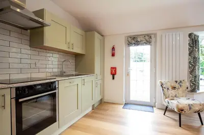 a kitchen with white cabinets and a chair at Beautiful Cottage nr Perranporth Private Parking in Perranzabuloe
