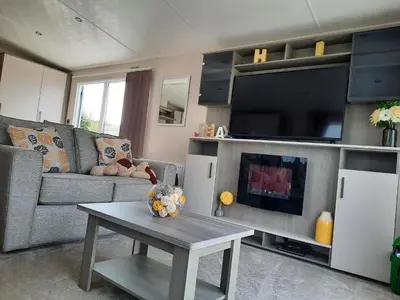 a living room with a couch and a tv and a table at Sunset retreat lodge with large wrap around decking in Newquay