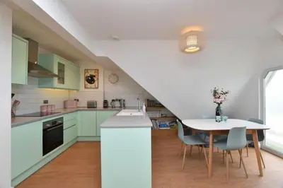 a kitchen with green cabinets and a table with chairs at Penthouse Sea View Newquay Fistral Beach 3 Min Walk in Crantock