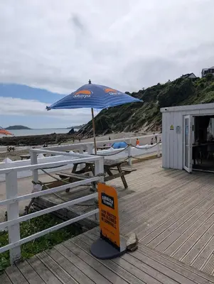 a picnic table with a blue umbrella on a beach at Luxury Sea View Chalet At Millendreath in Looe