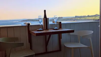 a table with wine glasses and a bottle on a balcony at C8 Bay Apartments - Fistral Beach View - Newquay in Newquay