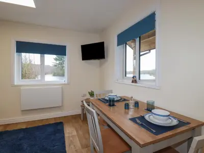 a dining room with a wooden table and two windows at Kingfisher Lodge in St Austell