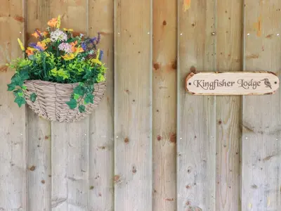 a basket of flowers and a sign on a wooden fence at Kingfisher Lodge in St Austell