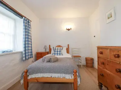 a bedroom with a bed and a dresser and a window at Swallow Cottage in St Austell