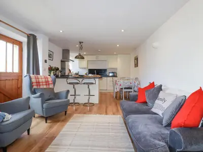 a living room with a couch and chairs and a kitchen at The Hayloft in St Austell