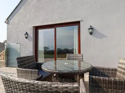 a patio with a table and chairs and a window at The Old Milking Parlour in Par