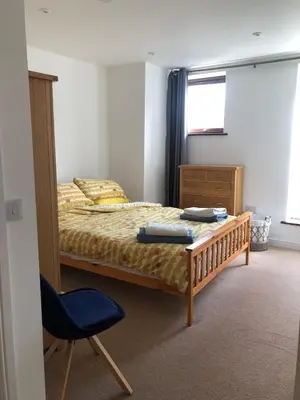 a bedroom with a bed and a blue chair at Captains Rest - Contemporary 4 bed apartment in Falmouth