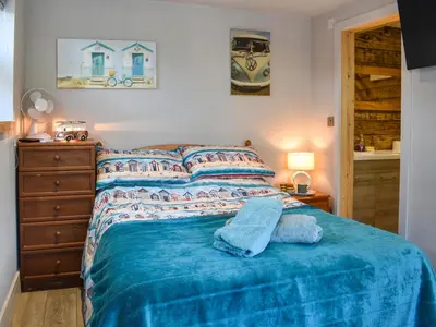 a bedroom with a bed with a blue blanket at Rosebud Beach Hut in Otterham