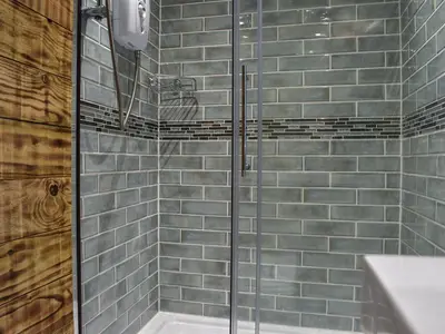 a glass shower in a bathroom with blue tiles at Rosebud Beach Hut in Otterham