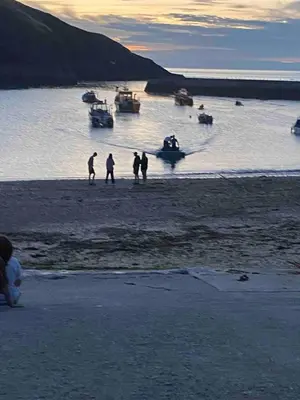 a group of people standing on a beach with boats in the water at The Porthole in Port Isaac