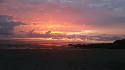 a sunset on a beach with the ocean at Headland Hideaway, Fistral Beach Newquay, Cornwall in Newquay