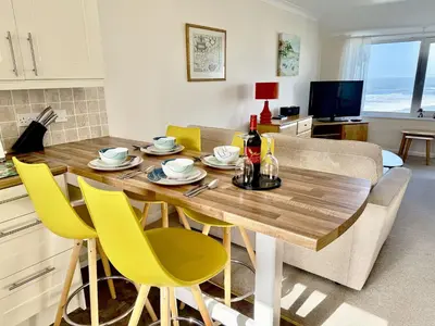 a kitchen and living room with a wooden table and yellow chairs at 16 Waters Edge, Atlantic Breezes in Newquay