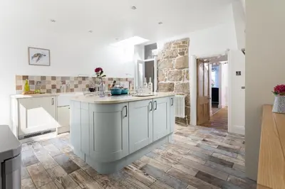 a kitchen with white cabinets and a wooden floor at Pendunes - Spectacular views, turquoise sea, love Cornwall in St Ives