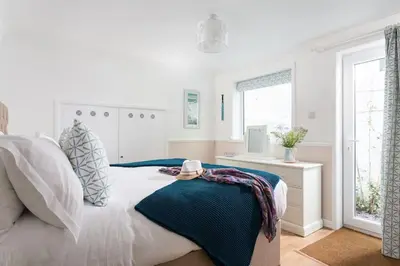a white bedroom with a bed and a window at Pendunes - Spectacular views, turquoise sea, love Cornwall in St Ives