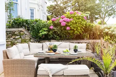 a patio with a table and chairs and pink flowers at Pendunes - Spectacular views, turquoise sea, love Cornwall in St Ives