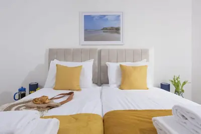 a bedroom with two beds with white and yellow pillows at 1 Island Reach in Newquay