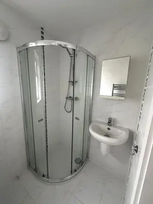 a white bathroom with a shower and a sink at Stylish beachfront penthouse in Perranporth
