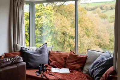a couch with pillows in front of a large window at Riverside barn on private wildlife estate in Washaway