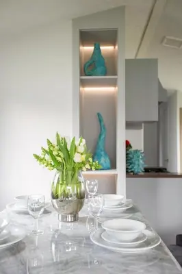 a table with plates and glasses and a vase with flowers at The Vacation, Cozy Static Caravan in Newquay in Newquay