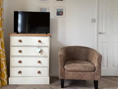 a chair sitting next to a dresser with a television on it at 85 Strawberry Hill Hayle in Hayle