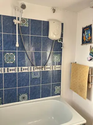 a bathroom with a tub and a shower with blue tiles at Cornish Cottage in Newquay