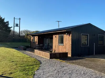 a small black building with a porch on a gravel driveway at Wheal Rock - Luxury 2 Bed Lodge in St. Agnes
