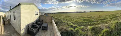 a small house on a deck next to a field at Meadow & Tide in St Merryn