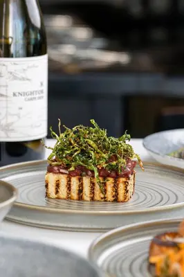 a piece of food on a plate next to a bottle of wine at St Moritz Hotel Apartments in Polzeath