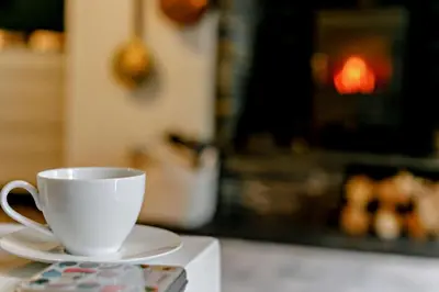 a white cup and saucer on a table with a fireplace at 2 Bed in St. Minver oc-p27580 in Saint Minver